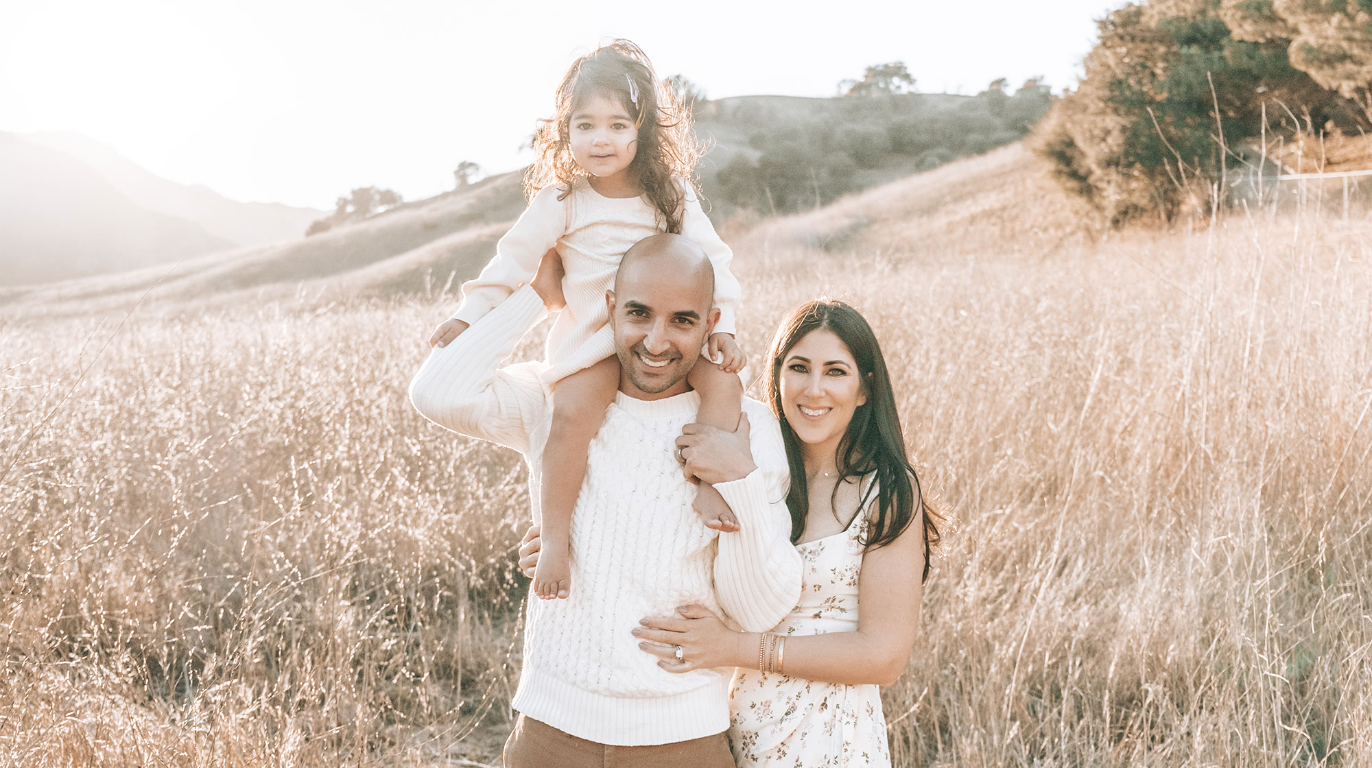 Professional photo of Jonathan beside his wife and daughter on his shoulders standing near hill in the city of Calabasas